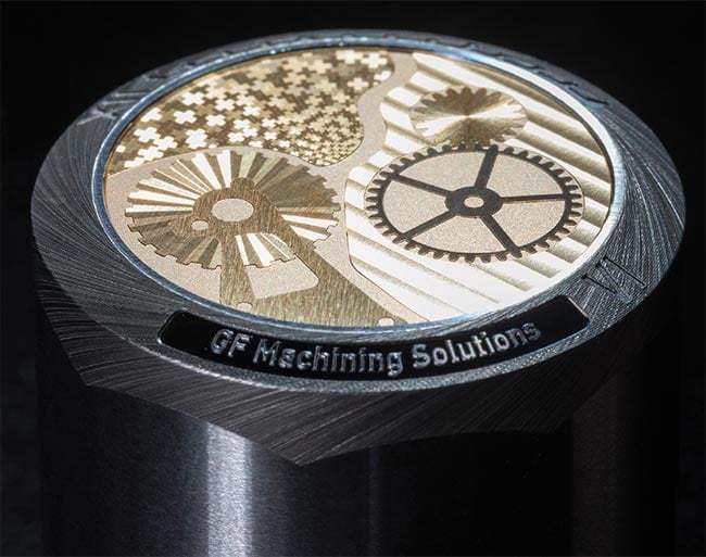 The centerpiece features a brass dial, engraved and decorated with a femtosecond laser for superior quality and aesthetics (top). The stainless steel exterior showcases five-axis capabilities, with deep engravings in white and blue, complemented by laser brushing to integrate the bezel with the outer cylindrical surface.  An image of a glass substrate processed using direct laser interference processing (DLIP) with a spatial period of 4 µm (bottom). Courtesy of GF Machining Advanced Solutions.