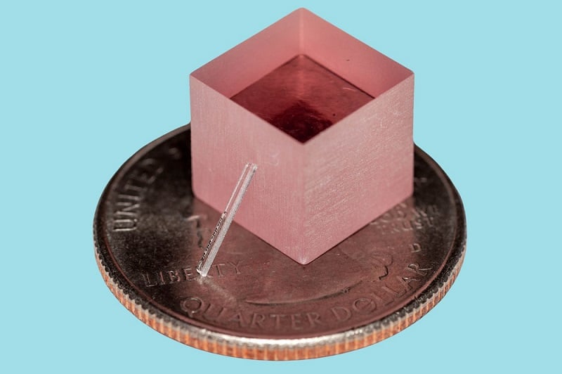 The researchers’ Ti:sapphire laser is chip-scale four orders of magnitude smaller (10,000x) and three orders less expensive (1,000x) than other Ti:sapphire laser. Here, it is depicted leaning against a block of Ti:sapphire and sitting on a quarter. Courtesy of Yang et al., Nature.