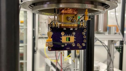 Close-up view of a superconducting nanowire single photon detector (SNSPD) mounted on a printed circuit board inside the cryostat at the Fermilab Test Beam Facility. This device was used in the first successful demonstration of high-energy proton detection using SNSPDs. Courtesy of Argonne National Laboratory/Sangbaek Lee.