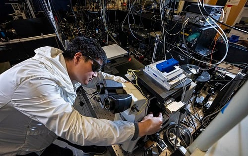 Researcher Xiao Qi in the laser room at the Molecular Foundry. Qi used the setup to develop a new optical computing material from nanoparticles that exhibit a phenomenon known as photon avalanching, in which a small increase in laser power results in a giant, disproportionate increase in the light emitted by the nanoparticles. Courtesy of Marilyn Sargent/Berkeley Lab.