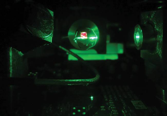 A green laser shines on a nitrogen-vacancy (NV)-center diamond. This excitation polarizes the spin system and results in the red light emission. The spin state determines the intensity of this photoluminescence. Courtesy of SBQuantum.