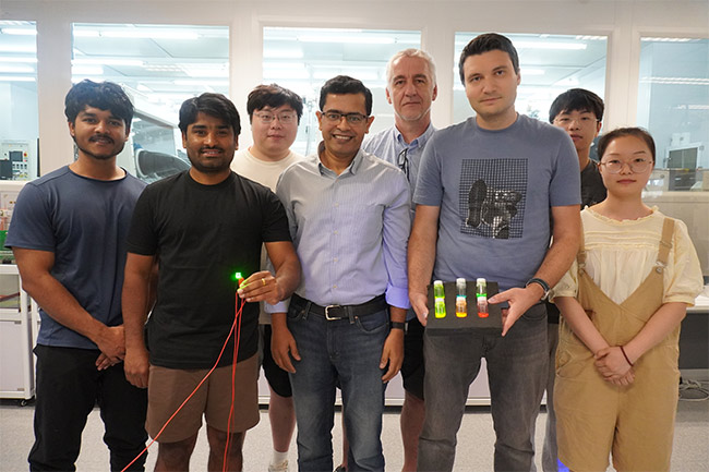 A group photo of Abhishek K. Srivastava (first row, center), Maksym Prodanov (first row, second right) and Ph.D. candidate Kumar Mallem (first row, second left) with members of their research team. Prodanov holds three bottles with quantum rod materials while Mallem holds a green emitting QRLED sample. Courtesy of Hong Kong University of Science and Technology. 